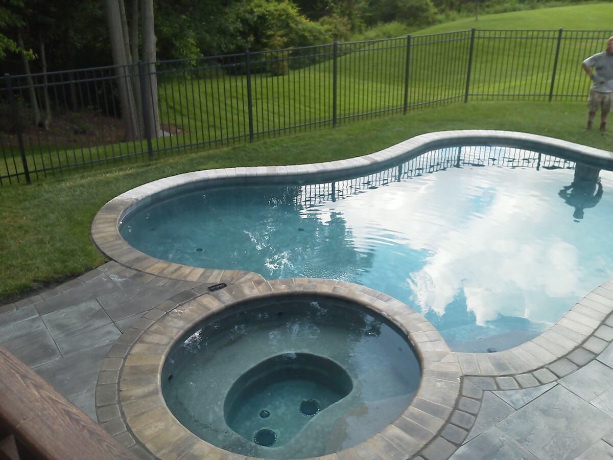 Pool with hot tub, patio, grass, and a fence